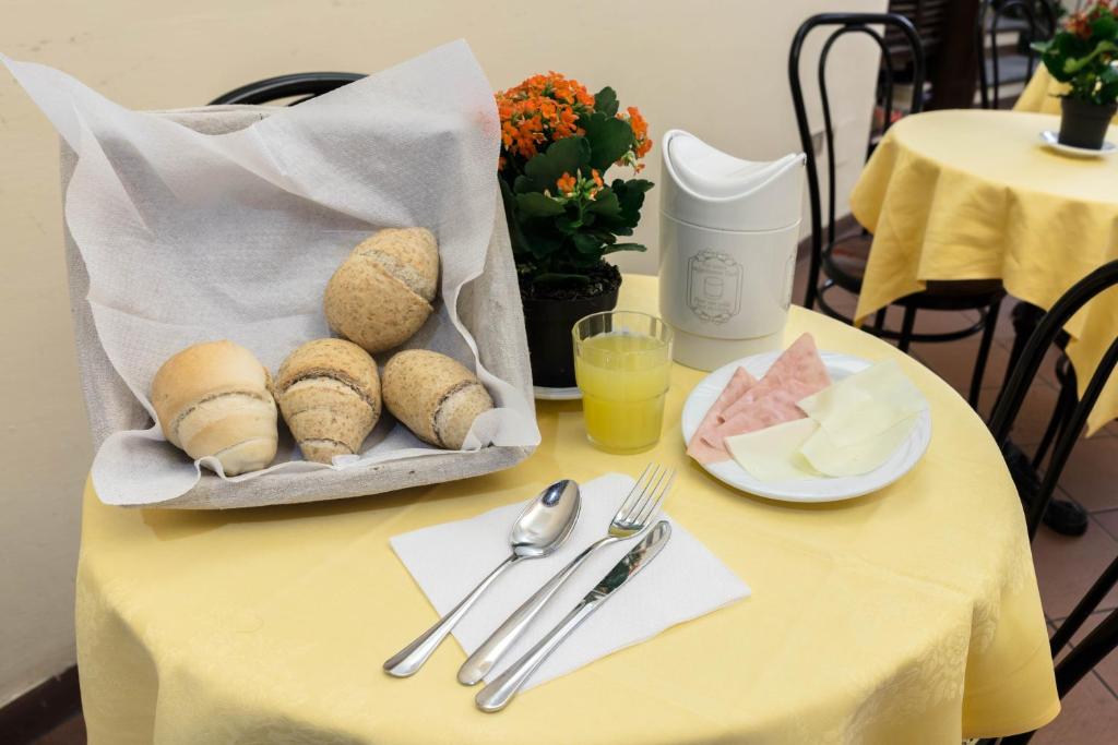 Brots maizes grozā kopā ar šķēlēm no gaļas un siera, glāze sulas un ziedu pods uz dzeltena galda.