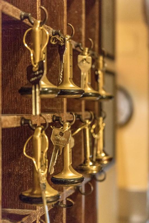 Atslēgu organizators ar zeltainām atslēgām, kas ir piekārtas pie koka plauktiņa, radot vintage atmosfēru.