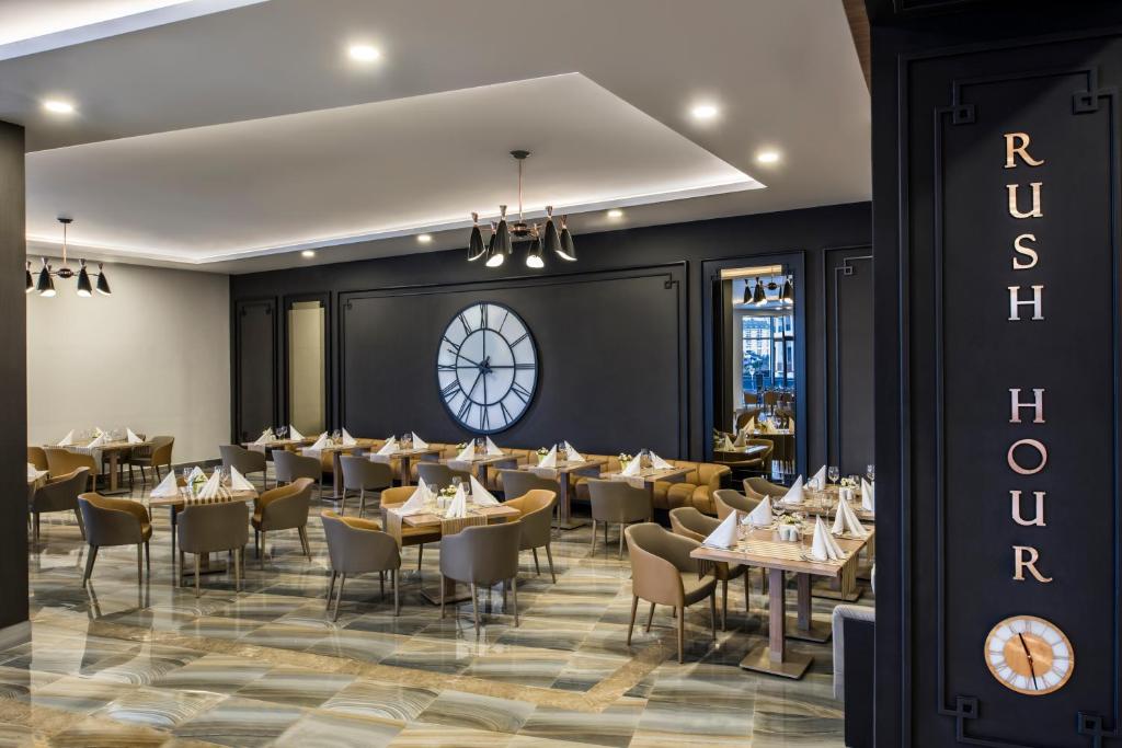 Mūsdienīgs restorāns ar elegantām galdiem un krēsliem, kas izkārtoti ap centrālo pulksteni. Sienas ir tumšas, radot kontrastu ar gaišo interjeru un akcentiem.