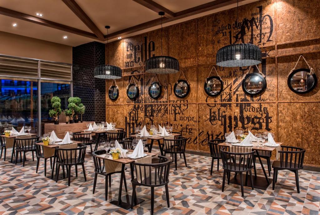 Mūsdienīgs restorāns ar elegantu interjeru, koka sienām un stilīgām lampām, kas papildina atmosfēru. Galdi ir saklāti ar baltām salvetēm un ziediem, radot viesmīlīgu noskaņu.