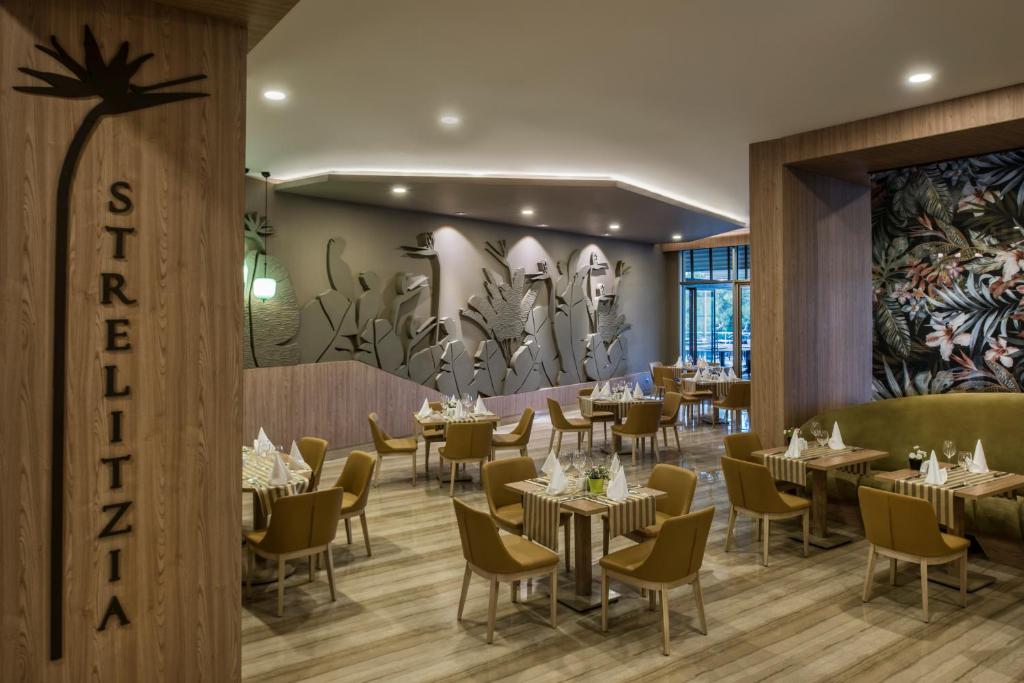 Mūsdienīgs restorāna interjers ar koka elementiem un zaļo augu motīviem uz sienām. Gaisma rada patīkamu atmosfēru, savukārt galdi un krēsli ir eleganti un ērti.