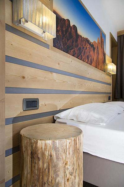 Mūsdienīgs guļamistabas interjers ar koka sienu, dekorētu ar horizontālām līnijām un apgaismojumu, kā arī dabīgu koka krēslu.