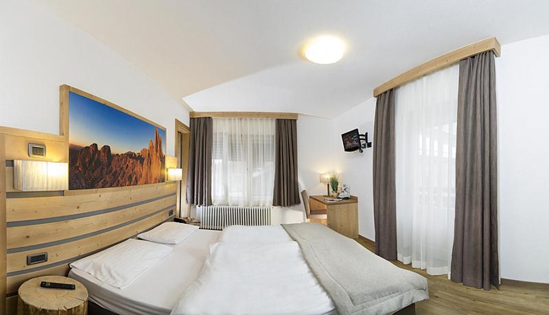 Mūsdienīgs viesnīcas numurs ar divguļamo gultu, koka apdari un skatu uz kalniem. Telpā ir dabiska gaisma, televizors un eleganta interjera detaļas.