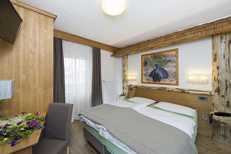 Mūsdienīgs viesnīcas numurs ar koka elementiem, ērtu gultu un dekoratīvu gleznu uz sienas. Telpā ir arī rakstāmgalds un ziedu kompozīcija.