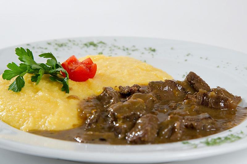 Garšīgs ēdiens ar mīkstu polentu un gaļas sautējumu, dekorēts ar pētersīļiem un tomātu. Ideāls izvēle siltām maltītēm.