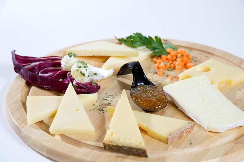 Siera šķēles uz koka dēļa kopā ar dārzeņiem un mērci, radot garšīgu uzkodu. Ideāli piemērots ballītēm vai svinībām.