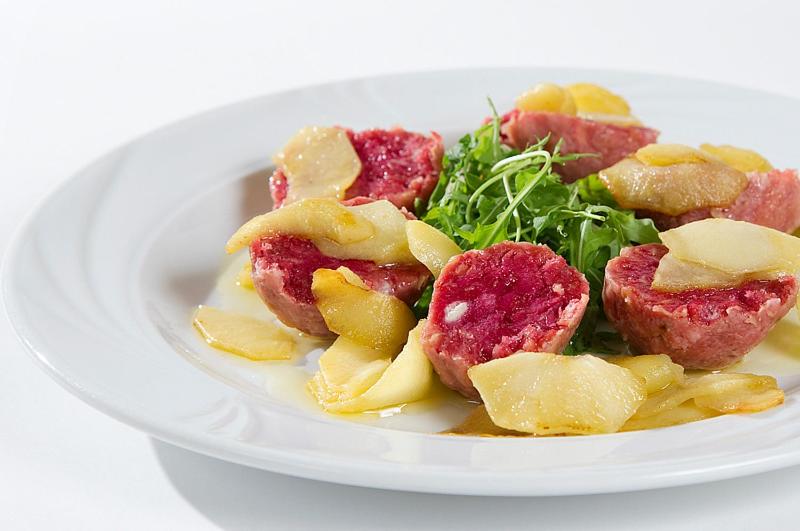 Gaļas ēdiens ar āboliem un zaļajiem salātiem, pasniegts baltā šķīvī.