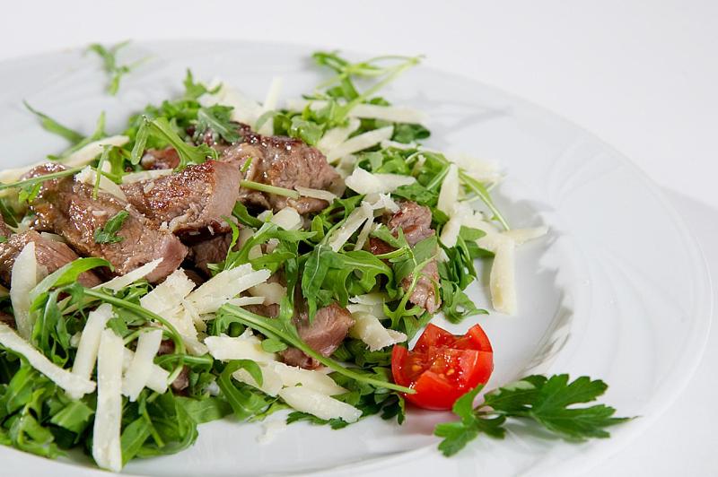 Svaiga rukola salāti ar ceptu gaļu un sieru, dekorēti ar tomātu un pētersīļiem.