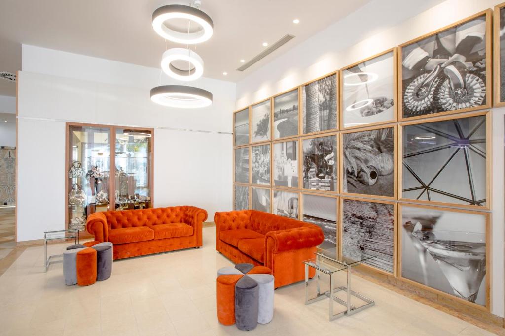 Mūsdienīgs interjers ar oranžām dīvāna komplektiem un oriģinālu fotogrāfiju sieniņu, kas piešķir telpai elegantu atmosfēru. Stils apvieno komfortu un estētiku.
