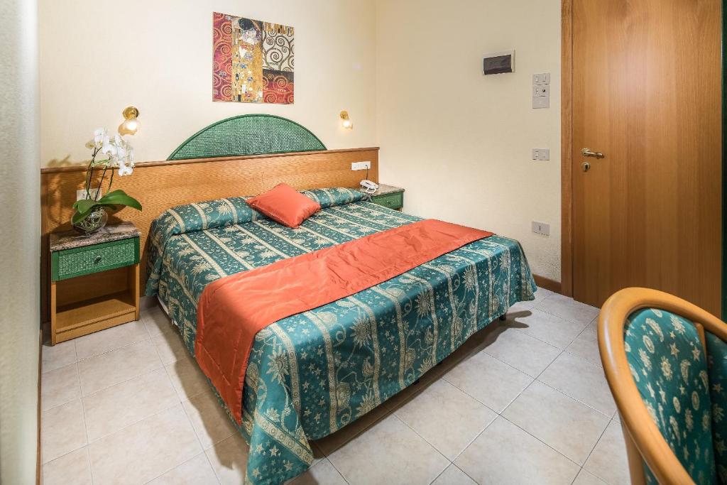 Maza, ērta viesnīcas istaba ar zaļo un sarkano tekstilu, parādīta ar gultu un nelielu galdiņu. Interjerā redzama mākslas bilde un orhidejas pods.