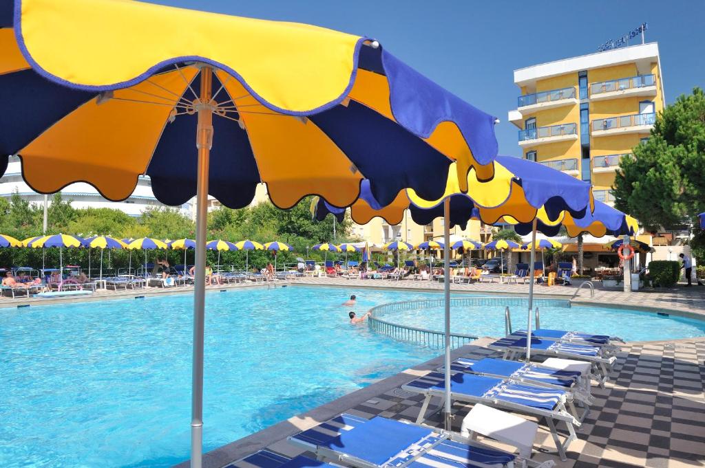 Baseins ar saules parapetiem un atpūtas krēsliem, apkārt cilvēki atpūšas un izbauda sauli. Vides atmosfēra ir relaksējoša un vasarīga.