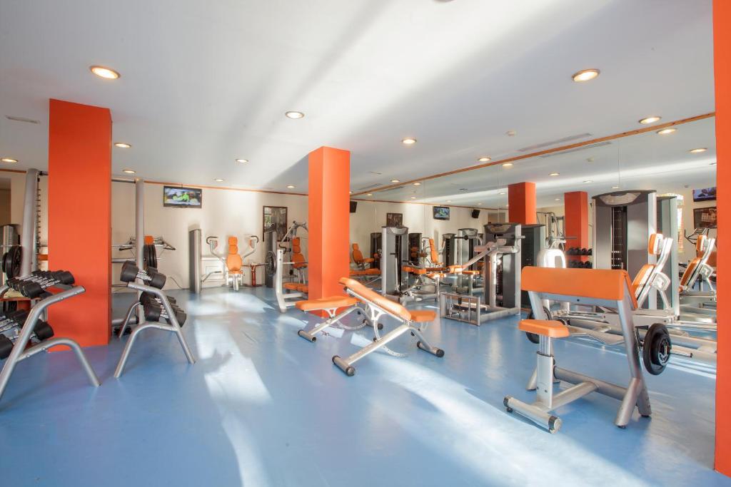 Sporta zāle ar modernām trenažieru iekārtām un oranžiem elementiem, kas rada dinamisku un motivējošu vidi treniņiem. Telpā ir daudz gaismas un brīva vieta vingrošanai.