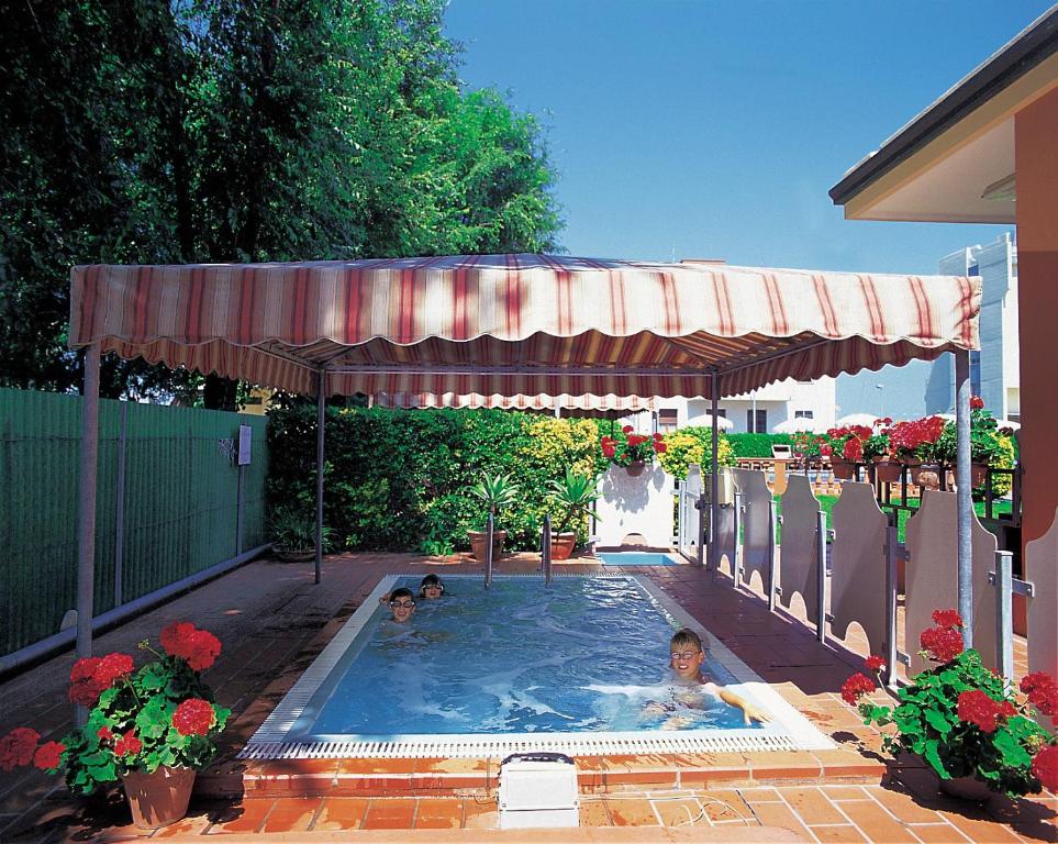 Baseins zem nojumes ar ziediem un bērniem, kuri priecājas par peldēšanu. Svaiga un saulaina atmosfēra, ideāla vasaras atpūtai.