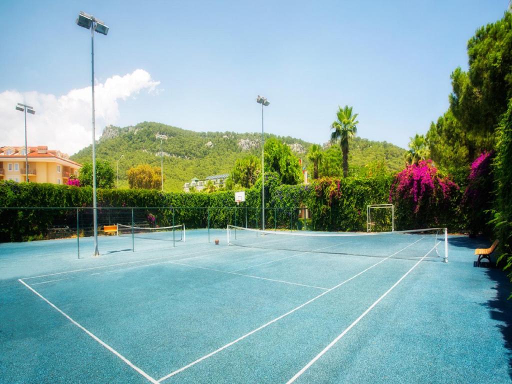 Tennisa korts ar zilu segumu, apzaļumotu apkārtni un kalnu fona. Ideāla vieta sporta aktivitātēm un atpūtai.