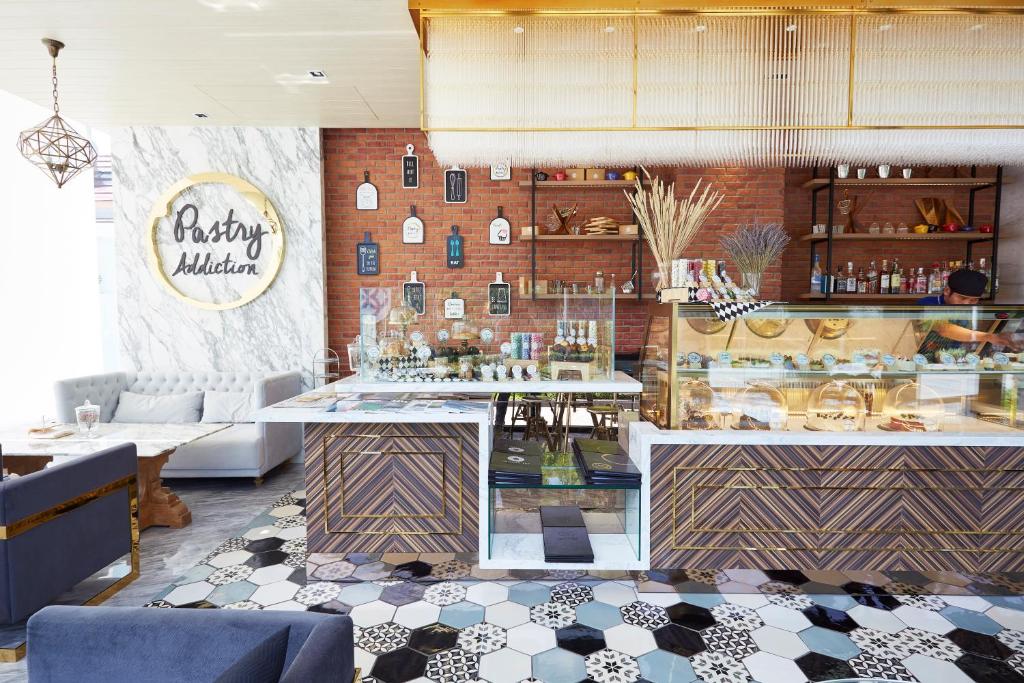Moderns konditorejas interjers ar stilīgu dekori un izvēli gardumu, kas veidoti ar dažādām flīzēm un dabīgām materiālām. Pastry Addiction zīme pie sienas piešķir vietai raksturu.