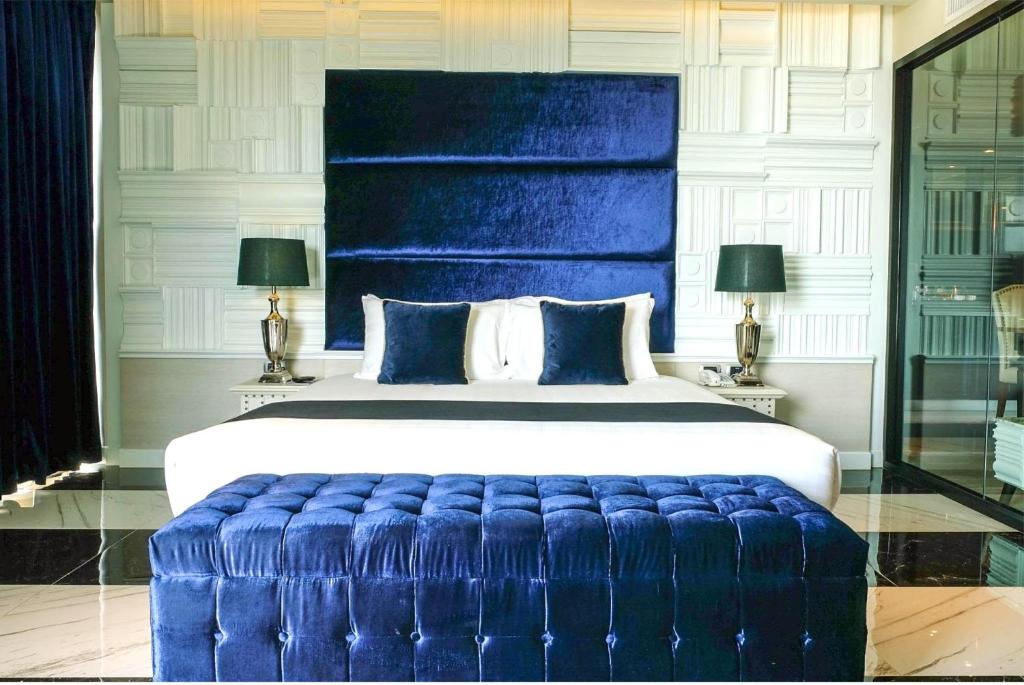 Mūsdienīgs guļamistabas interjers ar zilu aksesuāru un elegantu dizainu, ietverot gultu ar izteiksmīgu galvgali un stilīgu pufi.