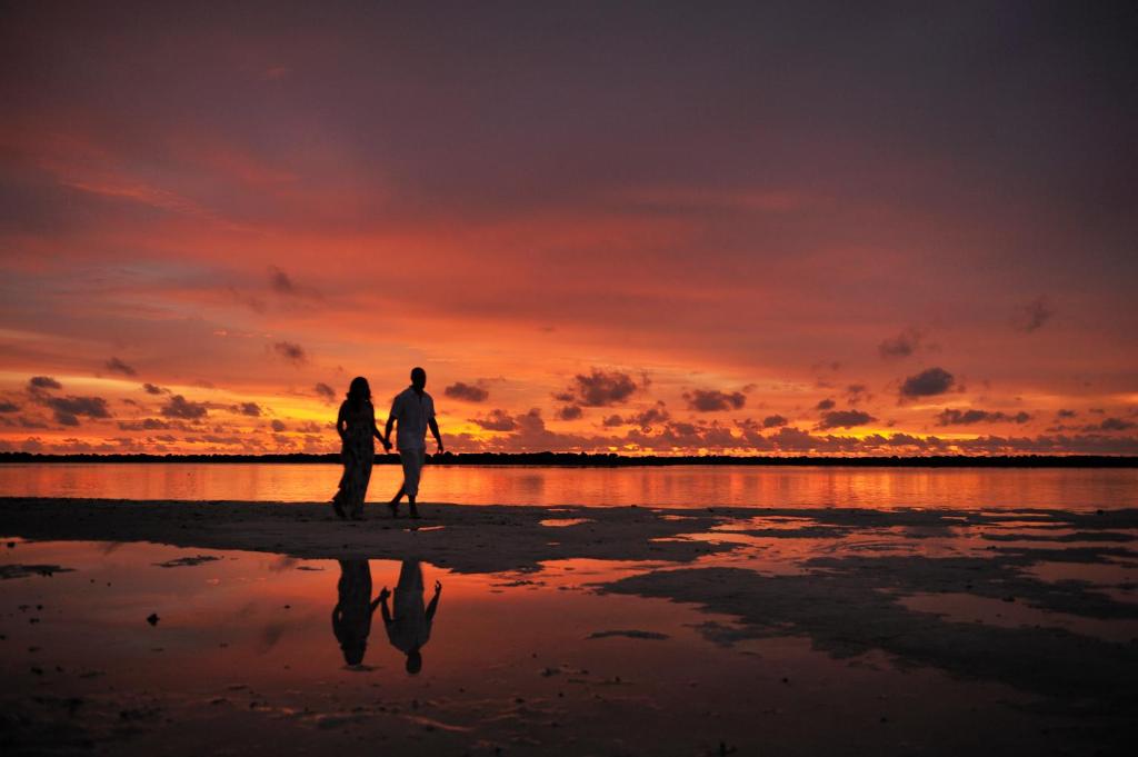 Romantisks saulriets, kur pāris pastaigā pa pludmali, atspoguļojoties ūdenī. Būtiska ainava ar košām krāsām un mierīgu atmosfēru.