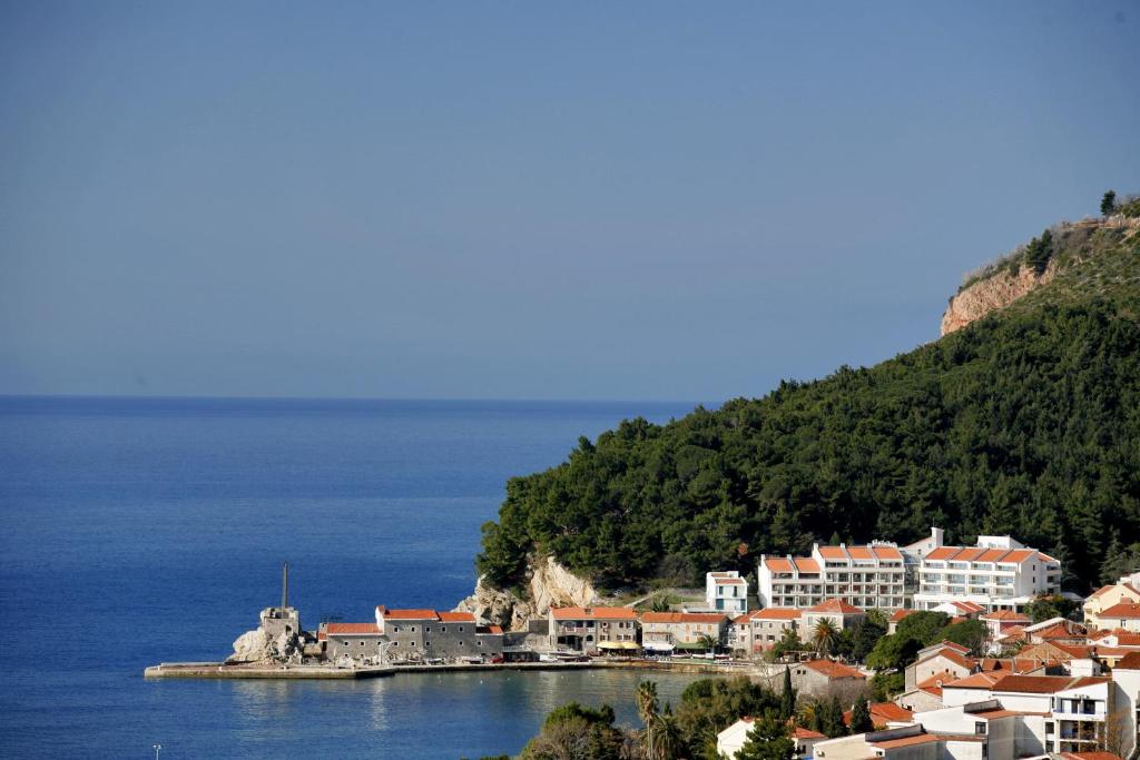 Jūras krastā esošs ciems ar baltiem māju jumtiem un zaļām kalnu nogāzēm fonā, kas veido gleznainu ainavu.
