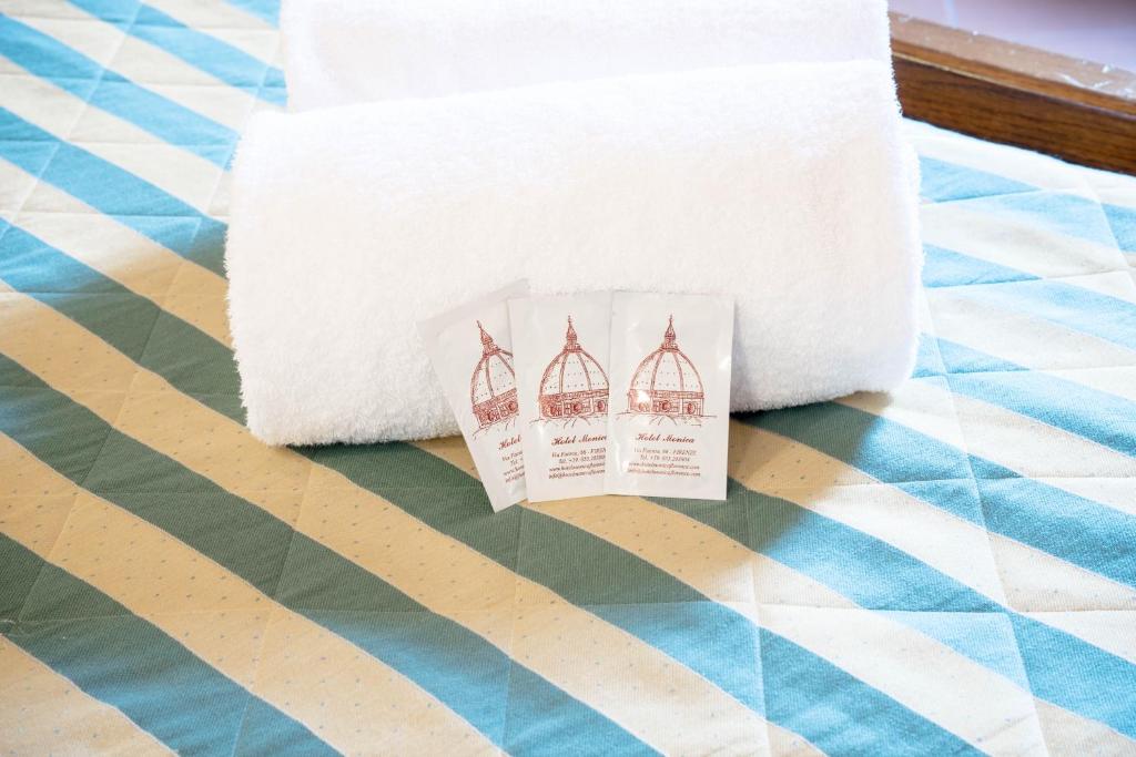 Baltas dvieļi un pakas ar zīmolu "Hotel Mexico" novietotas uz raibā gultas veļas.