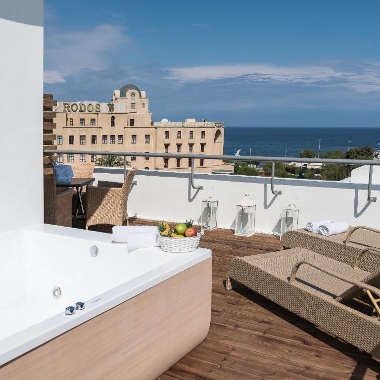 Luksusa terase ar džakuzi, no kuras paveras skats uz jūru un viesnīcu Rodos. Terasē ir sauļošanās krēslas un augļu grozs, radot relaksējošu atmosfēru.