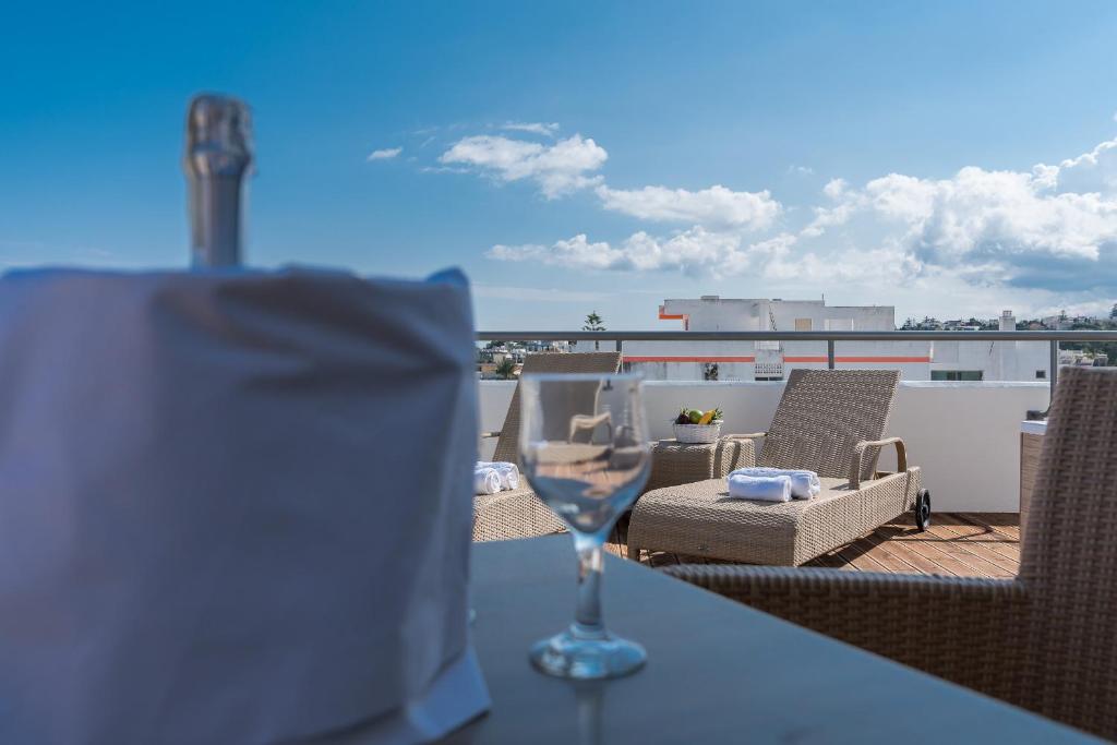 Terases skats ar šampanieša pudeli un glāzi, aizmugurē redzami atpūtas krēsli un saulains debesis ar mākoņiem.