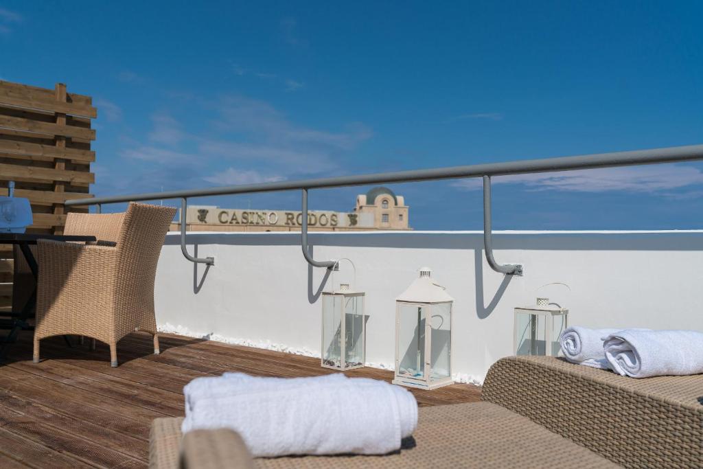 Terases skats ar brīviem saules krēsliem, galdu un lukturīšiem, kas izceļ relaksējošo atmosfēru. Fons ar zilo debesu un kazino ēkas siluetu.