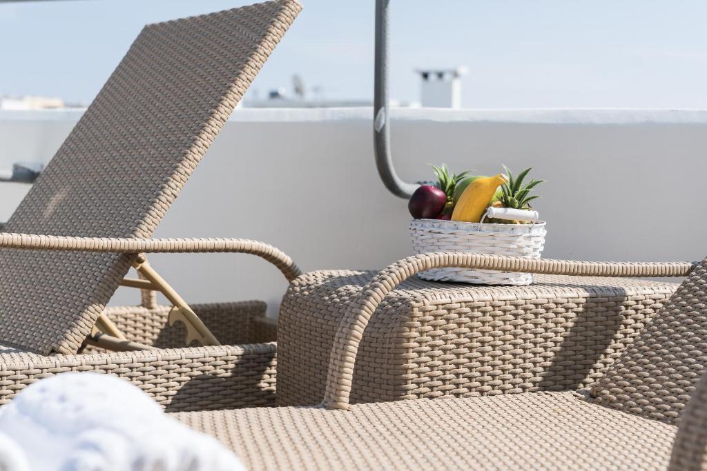 Sānu krēsls terasē ar augļu grozu, kurā iekļauti banāni un āboli, radot relaksējošu atmosfēru. Ideāls skats uz saulainu dienu.
