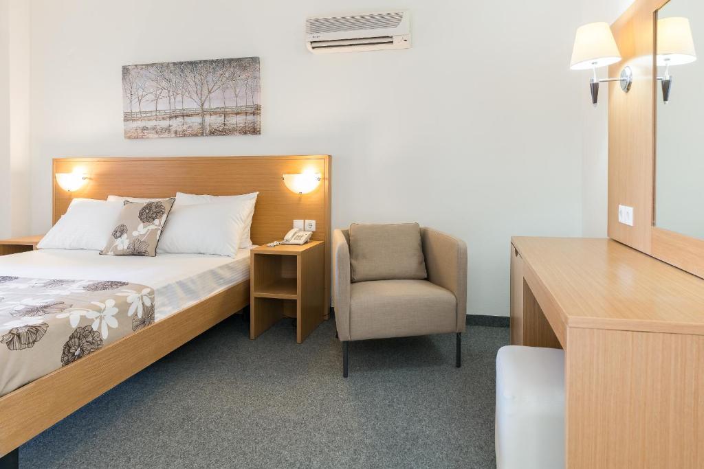 Mūsdienīga viesnīcas istaba ar divguļamo gultu, komfortablu krēslu un koka mēbelēm, kas piedāvā mājīgu atmosfēru un dabas motīvu uz sienas.