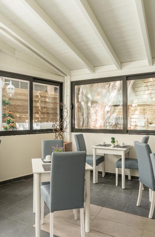 Gaiša un moderna kafijas istaba ar baltām galdiem un pelēkiem krēsliem, kas piedāvā patīkamu skatu uz dārzu caur lieliem logiem.