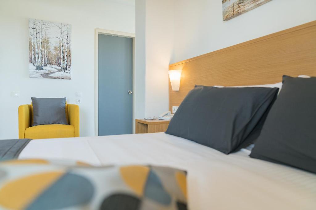 Mūsdienīgs viesnīcas numurs ar ērtu gultu, dzeltenu krēslu un mākslas darbu uz sienas, veidojot siltu un viesmīlīgu atmosfēru.