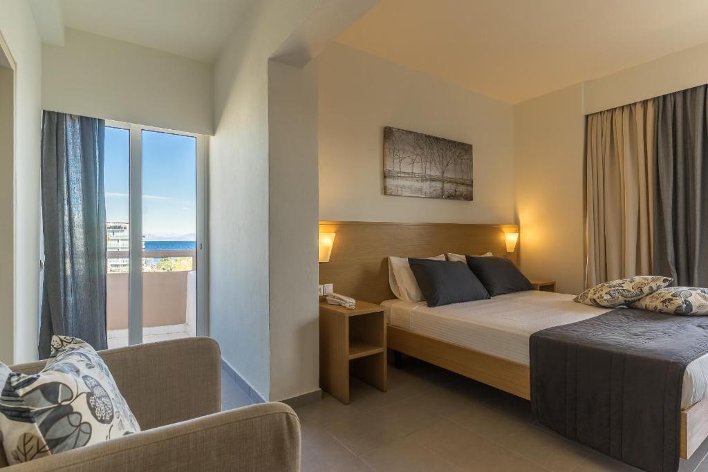 Mūsdienīga viesnīcas istaba ar divguļamo gultu, dīvānu un skatu uz jūru. Interjers ir gaišs un viesmīlīgs, ar mīkstām spilvenēm un dabīgām krāsām.