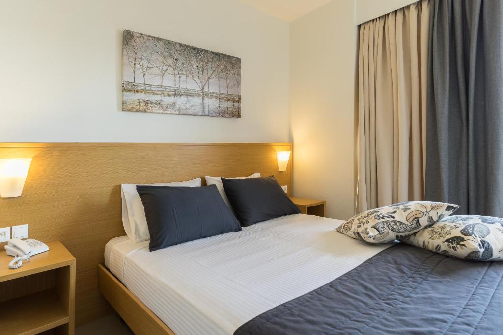 Mūsdienīga guļamistaba ar ērtu gultu, dekoratīvām spilveniem un gaismas elementiem, kas rada relaksējošu atmosfēru. Uz sienas ir mākslas darbs ar ainavu.