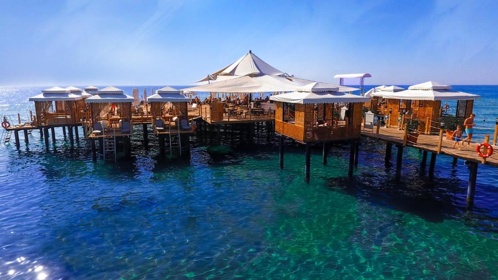 Koka piestātne ar nojumes, kas atrodas virs skaidra ūdens, kur cilvēki atpūšas un izbauda sauli. Ideāla vieta relaksācijai pie jūras.