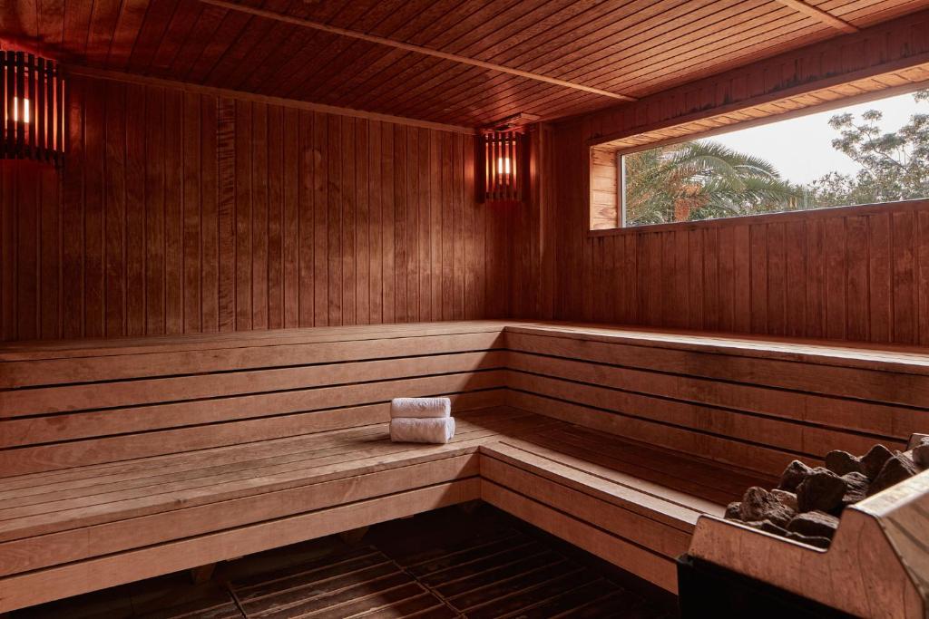 Koka sauna ar siltām gaismām un logu, caur kuru redzami zaļumi. Uz soliņa atrodas dvielis.