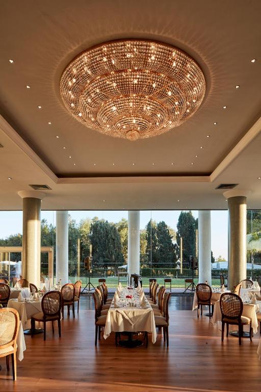 Elegants restorāns ar plašām stikla sienām, kas piedāvā skatu uz dārzu, rotāts ar greznu kristāla lustru un elegantām galdiem.
