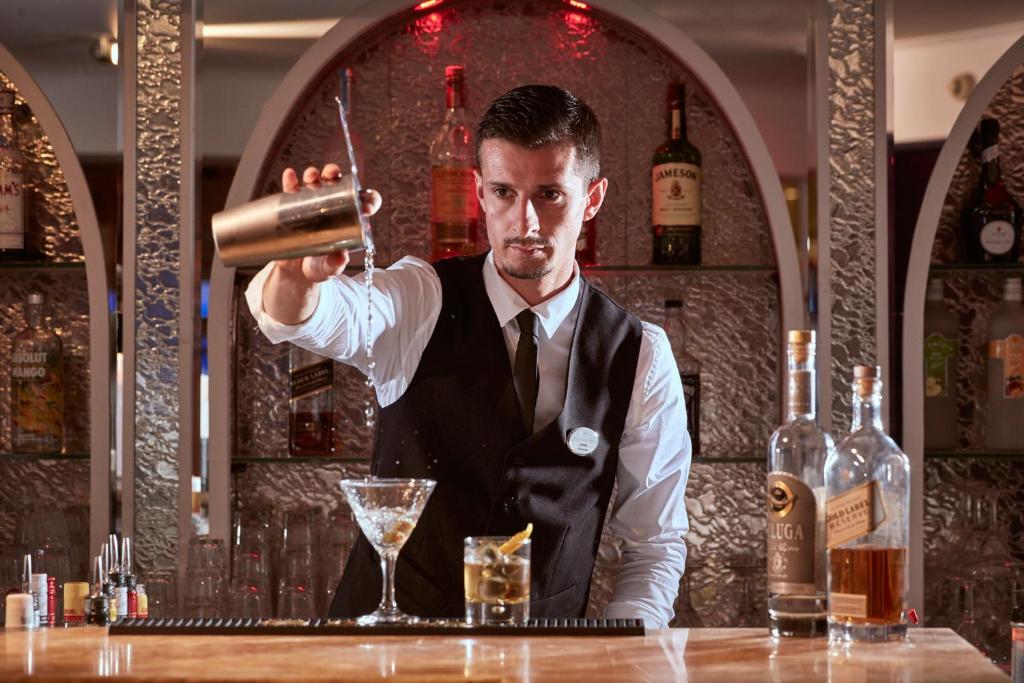 Bārmenis, kas sajauc dzērienu pie modernā bāra, fonā redzamas dažādas alkoholiskās dziras.