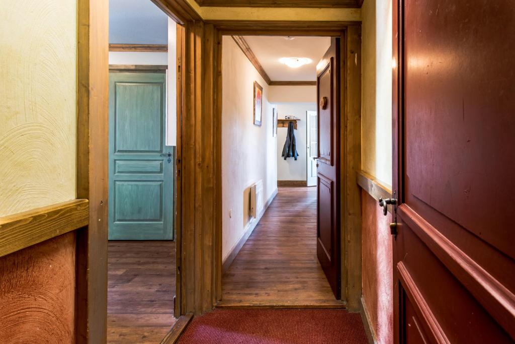 Gaišs un mājīgs gaiteņš ar koka apdari un krāsainām durvīm, kas ved uz dažādām telpām. Sienas rotā glezna, un pie sienas ir pakaramais apģērbam.