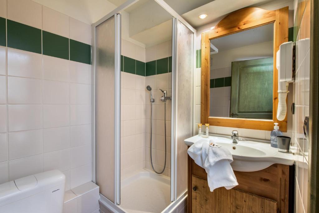 Vannas istaba ar dušu, baltām flīzēm un koka detaļām, kas rada mājīgu atmosfēru. Izsistās vannas piederumi un spogulis papildina telpas funkcionalitāti.