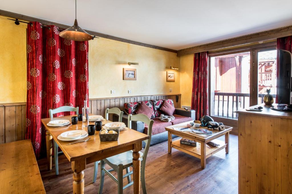 Mājīgs dzīvojamais istabas un ēdamistabas interjers ar koka mēbelēm, sarkaniem aizkariem un dabiskiem apgaismojumiem. Ideāla vieta relaksācijai un ģimenes kopā pavadītajam laikam.