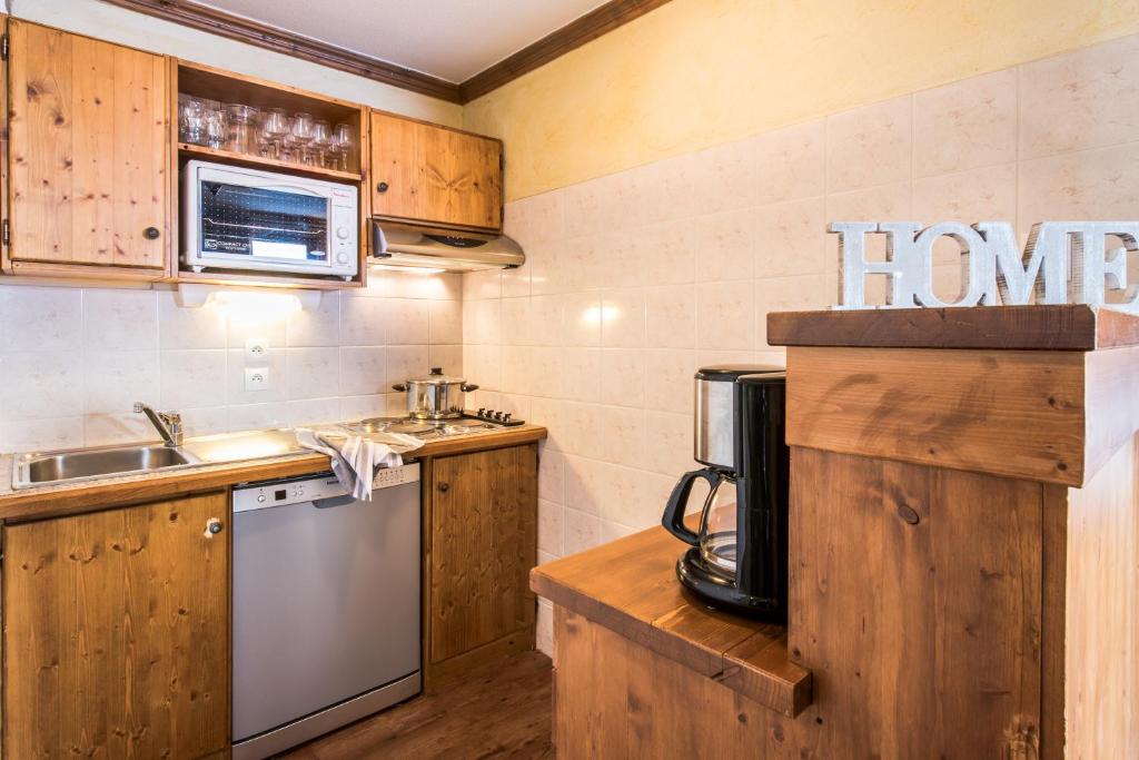 Virtuves telpa ar koka mēbelēm, mikroviļņu krāsni un trauku mazgājamo mašīnu. Uz galda ir kafijas automāts un dekoratīvs uzraksts 