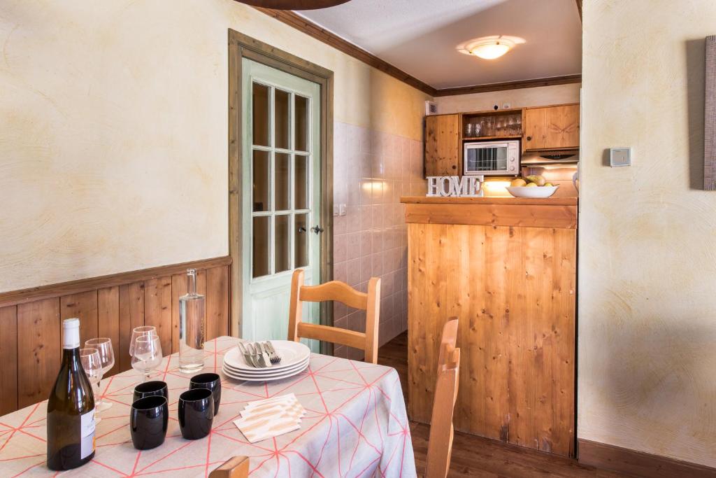 Mūsdienīga virtuve ar ēdamgaldu, kas klāts ar galda piederumiem un vīnu, siltās krāsās un dabīgā koka akcentiem. Interjers rada mājīgu atmosfēru.