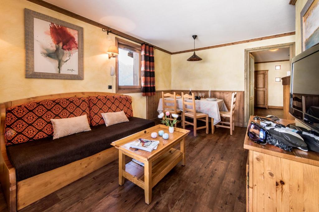 Mūsdienīgs viesistabas interjers ar dīvānu, koka galdu un ēdamgaldam piemērotām krēsliem. Uz galda ir ziedi un dažas grāmatas, bet uz sienas redzams mākslas darbs.