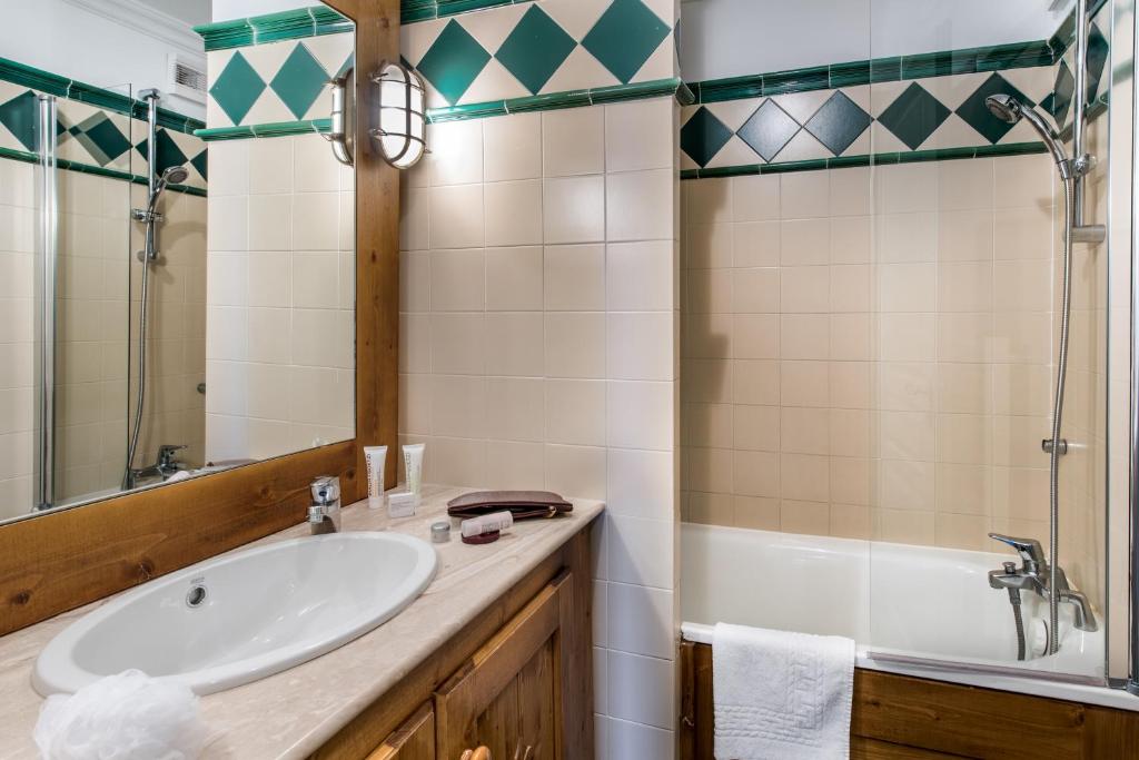 Mūsdienīga vannas istaba ar gaišām flīzēm un koka detaļām. Tajā ir duša, vanna, izlietne un kosmētikas piederumi uz letes.