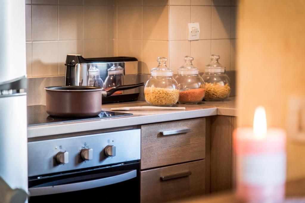 Mājas virtuve ar trauku, kas gatavojas vārīšanai, un stikla burkām ar makaronu un pākšaugu krājumiem. Siltas gaismas atmosfēra, kas rada mājīgu noskaņu.