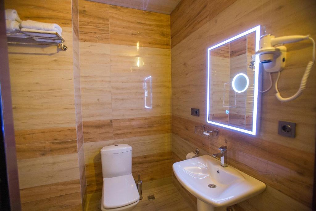 Mūsdienīgs un elegants vannas istabas interjers ar koka apdari, izsmalcinātu spoguli un higiēnas ierīcēm. Telpa ir gaiša un funkcionāla, nodrošinot komfortu un stilīgu atmosfēru.