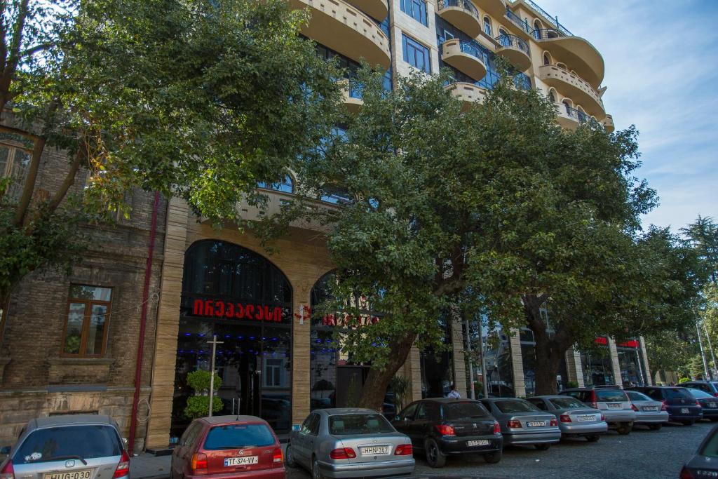 Mūsdienīga ēka ar balkoniem un lieliem logiem, kas atrodas blakus koku rindai un autostāvvietai. Redzama arī restorāna zīme.