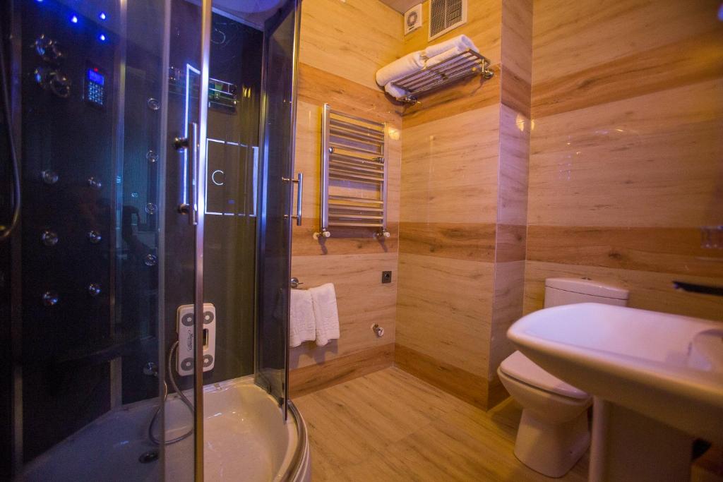 Mūsdienīga vannas istaba ar stikla dušu un siltām koka akcentiem, aprīkota ar mūsdienīgām ierīcēm. Telpa ir gaiša un eleganta, radot relaksējošu atmosfēru.
