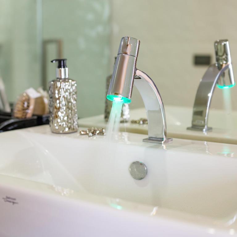 Moderns vannas jaucējkrāns ar LED apgaismojumu, kas strūklā izsūknē ūdeni. Svaigi izskatīgs izlietnes dizains ar dekoratīviem elementiem fonā.