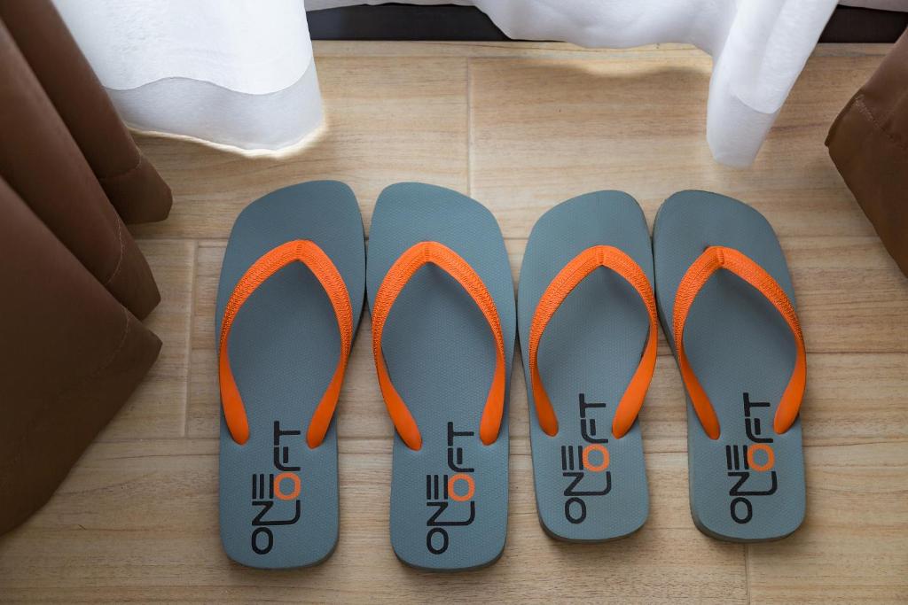 Četras pelēkas flip-flop čības ar oranžiem siksniņām, izkārtotas uz grīdas. Ideāli piemērotas vasaras atpūtai.