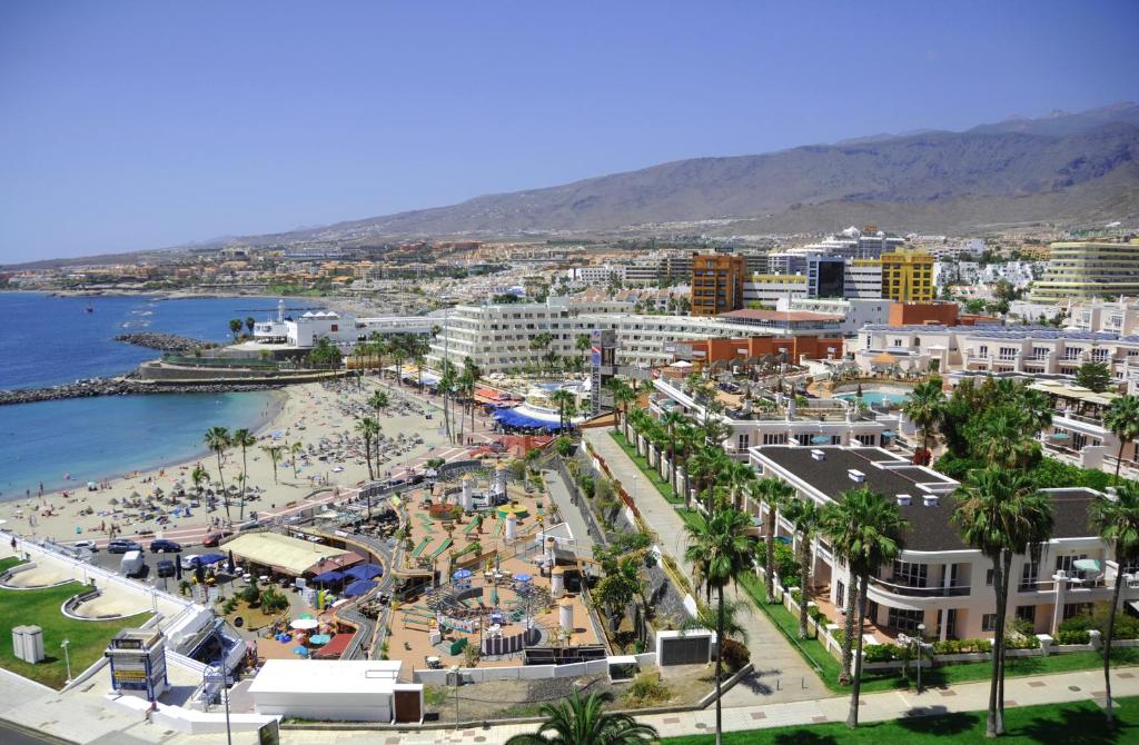 Sauļota pludmale ar atpūtniekiem, viesnīcām un kalnu fona Tenerifē. Skats uz krastmalu un pilsētas ainavu.